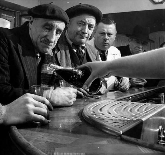 Vintage scene with men in berets at a bar, a hand pouring a drink, capturing a moment not in most history textbooks.