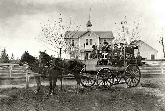 Historic photo of children in a horse-drawn school bus in front of a classic schoolhouse, highlighting rarely seen history.