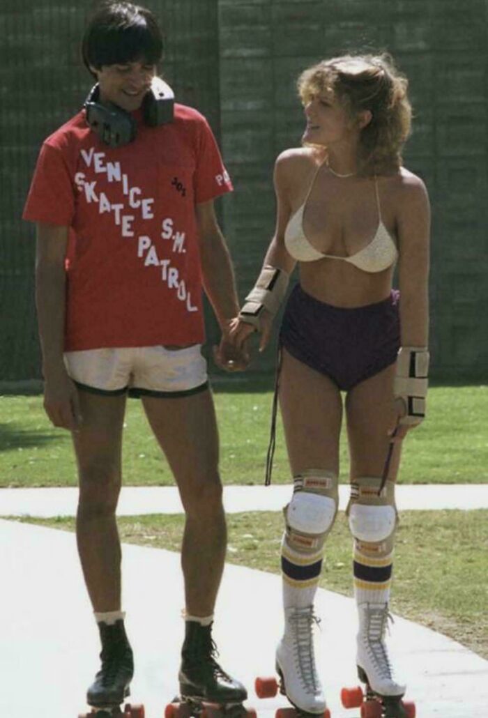 Two people roller skating in vintage outfits, holding hands, showcasing a rare historical scene.