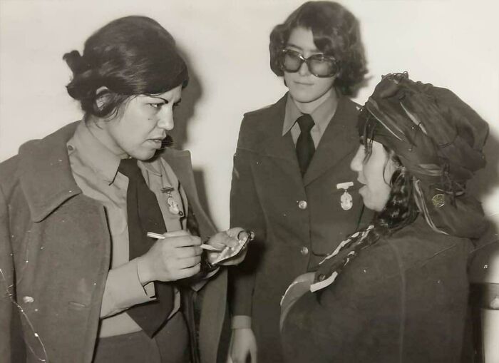 Two uniformed women taking notes from a person in a turban, historical context not typically seen in textbooks.