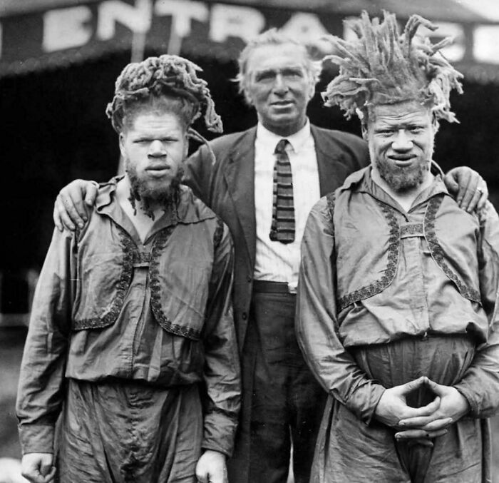 Two men with unique hairstyles and a man in a suit pose together in a historical photo not often seen in textbooks.