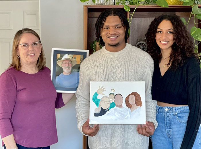 Three people celebrating viral Thanksgiving tradition, holding a portrait and painting.