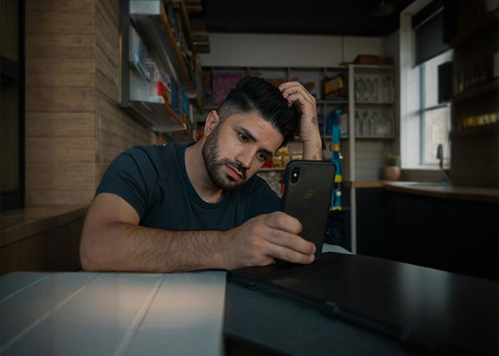Man sitting in a kitchen, looking thoughtfully at his phone, representing struggles men wish women knew.