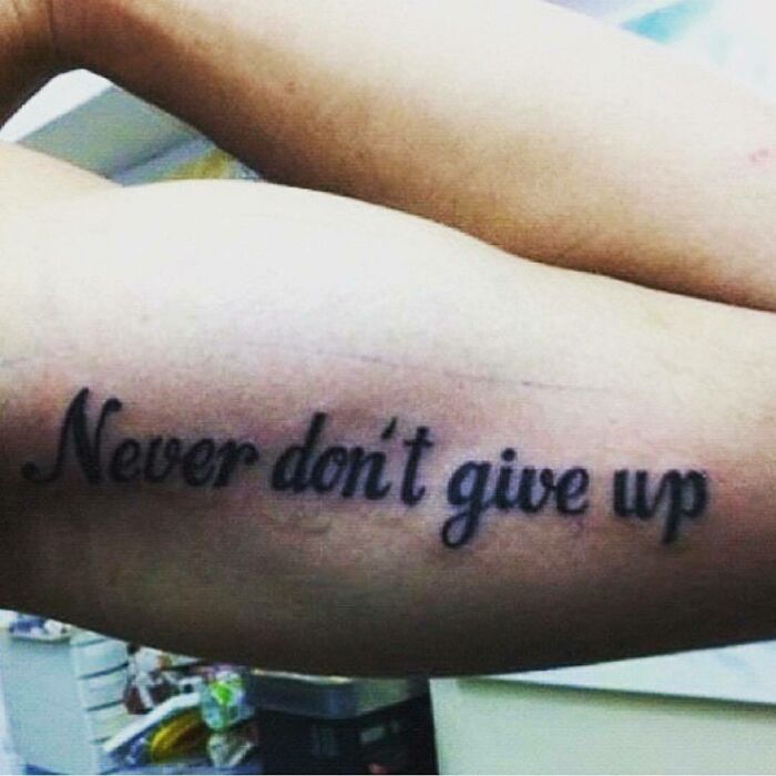 Tattoo on arm with typo: "Never don't give up," showcasing a permanent mistake.
