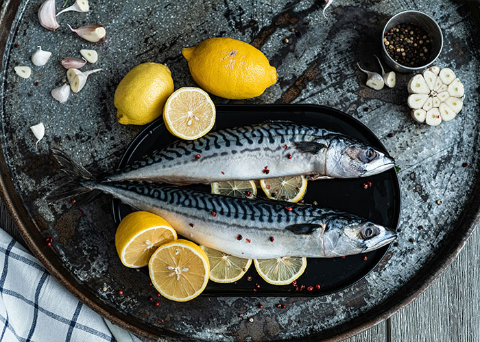 Fresh mackerel on a black plate with sliced lemons and garlic, illustrating a common petty reason that led to divorce.