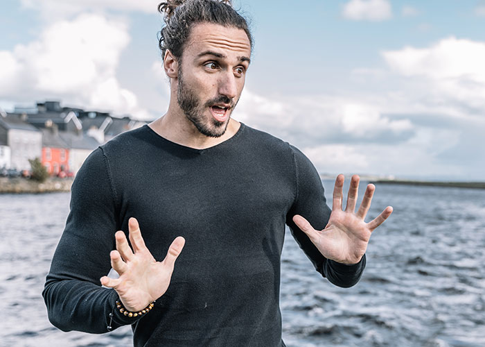 Man in a black shirt by the water expressing surprise, highlighting men's struggles in communication.