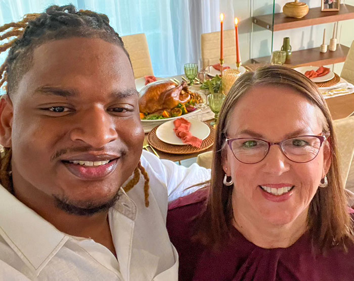 Jamal and Wanda are smiling in front of a table set for Thanksgiving, celebrating their 8th holiday together after an accidental SMS.