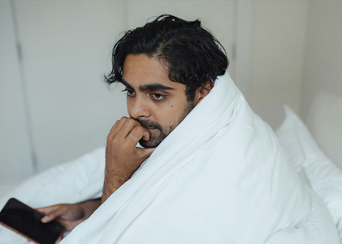 A person under a white blanket looks pensive, holding a phone, possibly reacting to savage insults.