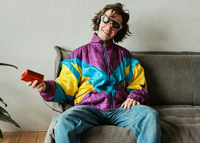 Man in a colorful '90s windbreaker with retro sunglasses and a cassette player, embodying nostalgic trends.