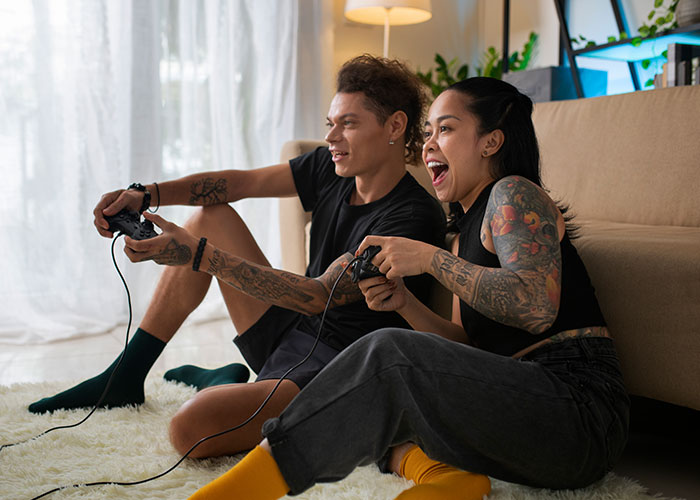 Two people with game controllers, embracing nostalgia, enjoying a gaming session reminiscent of '90s and '00s trends.