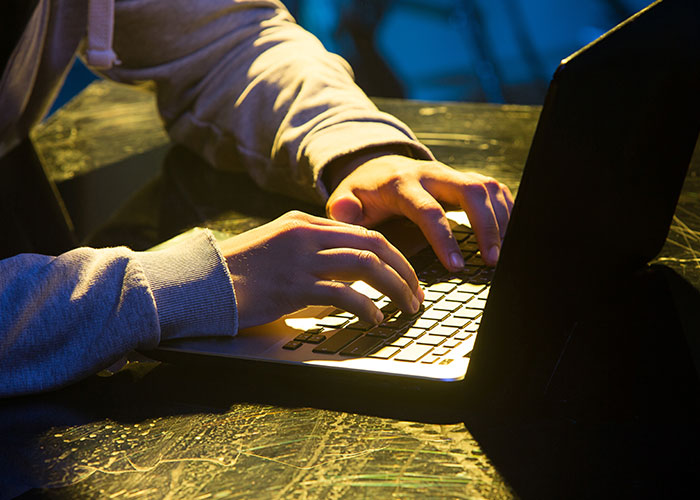 Person in ’90s fashion typing on laptop in a dimly lit room, highlighting retro trends.