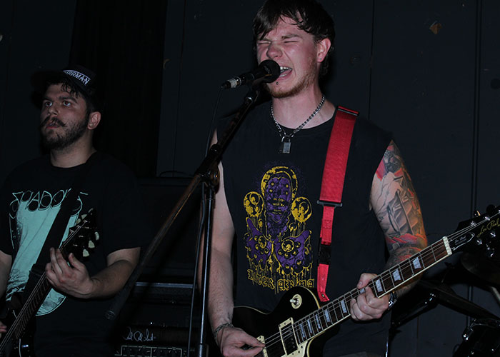 Musician with tattoos passionately performing on stage, representing '90s and '00s trends in rock music.