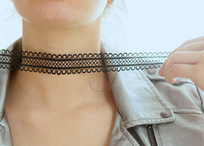 Person wearing a black choker necklace from '90s fashion trends, paired with a gray leather jacket.