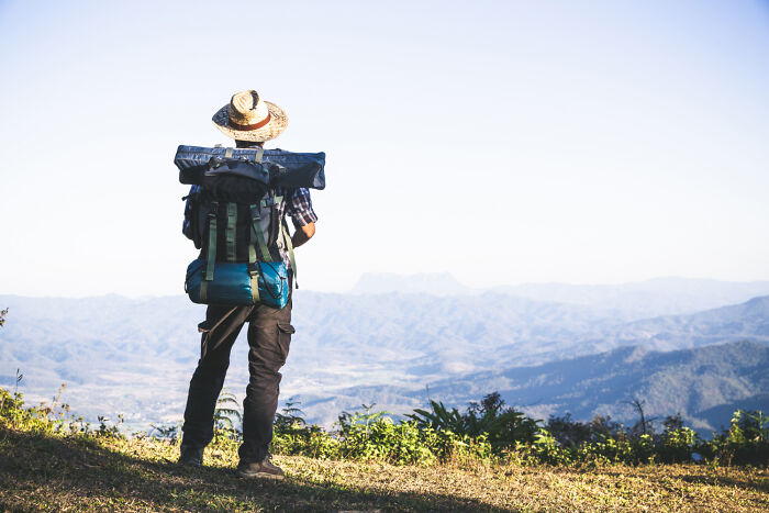 Backpacker on a mountain edge, taking a risky decision to explore the wilderness, with a hat and large backpack.