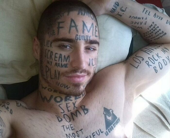 Man with tattoos covering his face and body, featuring various words and phrases.