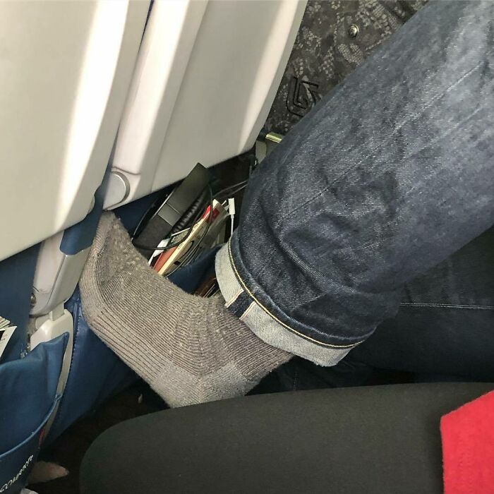 Sock-clad foot resting on airplane seat back, illustrating annoying plane passengers.