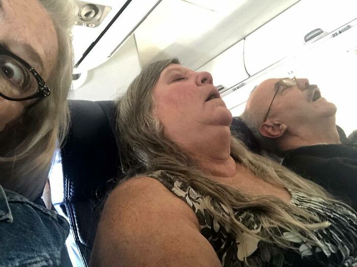 Passengers sleeping on a plane, one looking annoyed in the foreground.