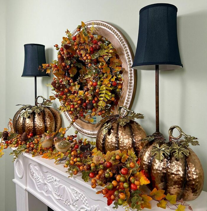 Thanksgiving home decor with metallic pumpkins, autumn leaves, and wreath on a mantelpiece, enhanced by elegant lamps.