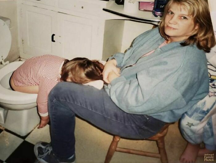 Awkward family photo of a child with head in toilet and a seated woman looking at the camera.