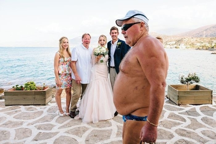 Man in swimsuit photobombs family at wedding by the sea; a viral family photo moment.