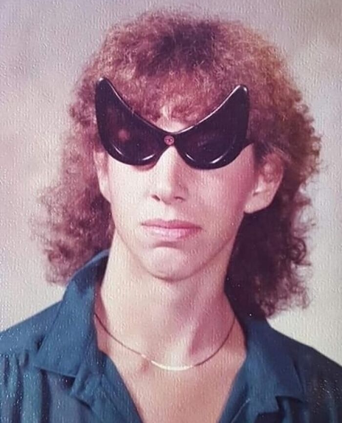 Person with curly hair wearing unique black sunglasses, capturing a humorous family photo moment.