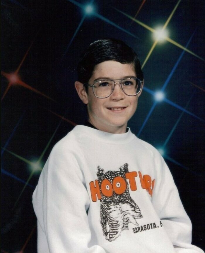 A kid in a vintage sweater and glasses poses awkwardly for a family photo with a laser backdrop.