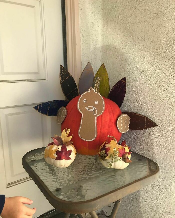 Thanksgiving home decoration with a turkey-themed pumpkin centerpiece and leaf accents on a glass table.