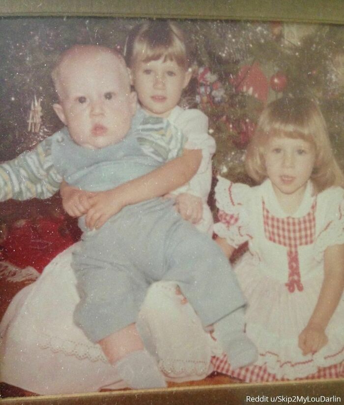Three siblings pose in front of a Christmas tree in a vintage family photo.