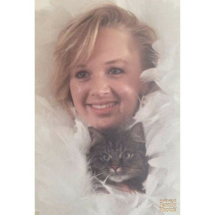Woman smiling with a cat, surrounded by soft white feathers, capturing an awkward family photo moment.