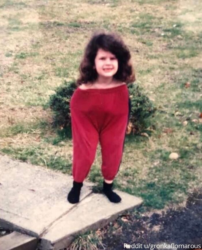 Child wearing oversized red pants standing on a lawn, smiling awkwardly; a viral family photo moment.