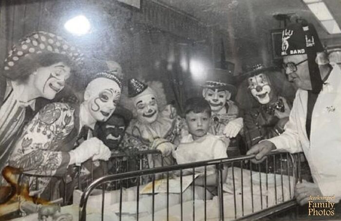 Awkward family photo of a child in a hospital bed surrounded by clowns and an older man wearing a fez.