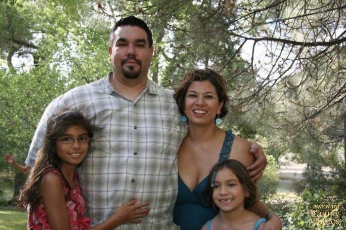 Awkward family photo of a smiling group outdoors, surrounded by trees and greenery.