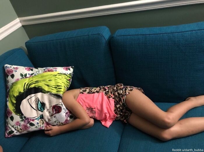 Child on a blue couch with a pillow covering their head, blending with pillow art for a humorous family photo gone viral.