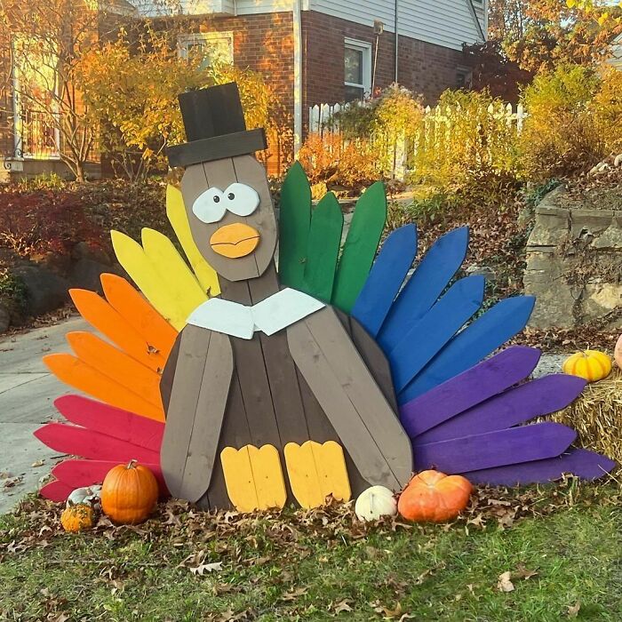 Thanksgiving home decoration featuring a colorful wooden turkey with pumpkins in a garden setting.