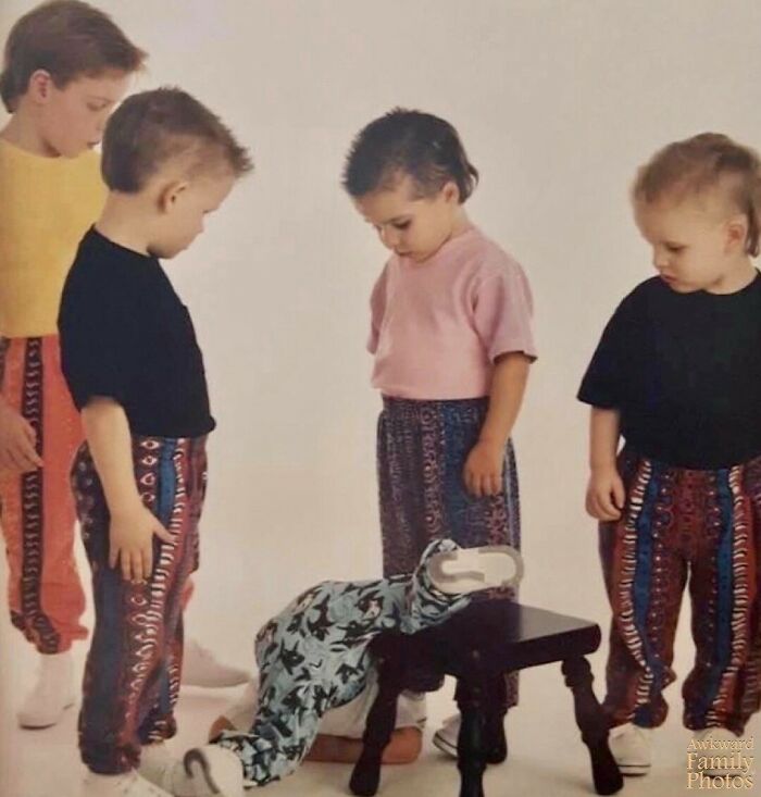 Four children in colorful outfits looking at another child who has fallen off a chair, creating an awkward family photo moment.