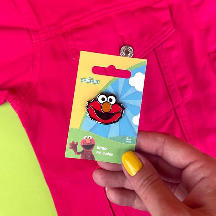 Elmo enamel pin badge on packaging held in front of pink jacket.