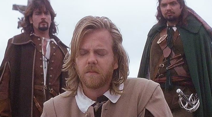 A famous trio from The Three Musketeers, featuring Athos, Porthos, and Aramis in period costumes, with serious expressions in a somber outdoor setting.