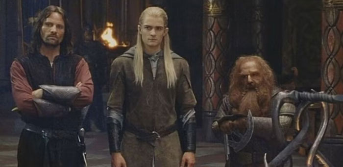 A famous trio from The Lord of the Rings, featuring Aragorn, Legolas, and Gimli standing together in a grand hall with serious expressions.