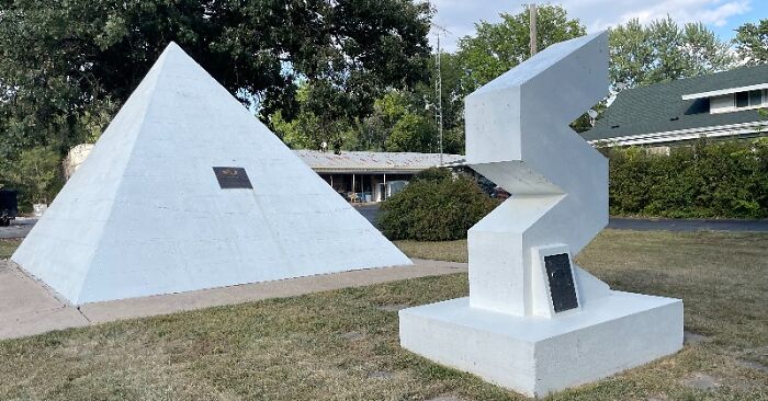 White pyramid and abstract sculpture in a grassy area, representing historical time capsules.