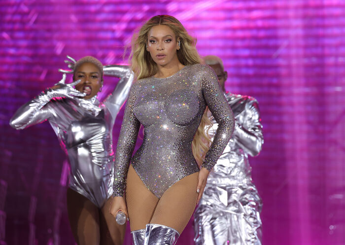 Popstar Beyonc&eacute; performs in a dazzling silver outfit with vibrant pink background and backup dancers.