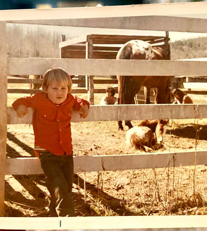 Child in orange jacket by a wooden fence with animals, related to Josh Brolin's wildlife stories.