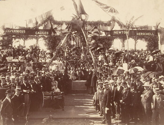 Historical time capsule ceremony with a large crowd, featuring banners of famous scientists.