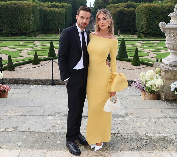 A man in a suit and a woman in a yellow dress stand together in an elegant garden setting. A man in a suit and a woman in a yellow dress stand together in an elegant garden setting.