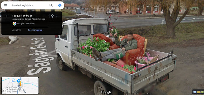 Man relaxing on a sofa in the back of a truck, surrounded by plants, captured on Google Street View.