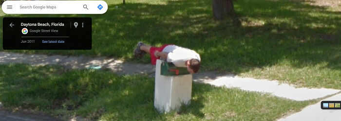 Person lying face down on a mailbox in a humorous scene captured by Google Street View in Daytona Beach, Florida.
