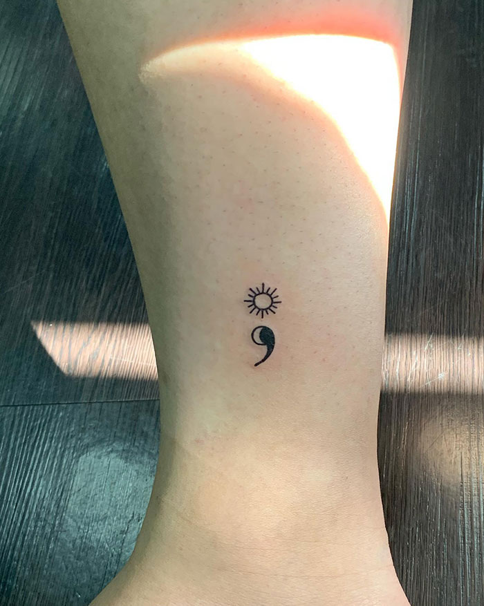 Lower leg semicolon tattoo with a sun symbol above, representing hope and resilience.