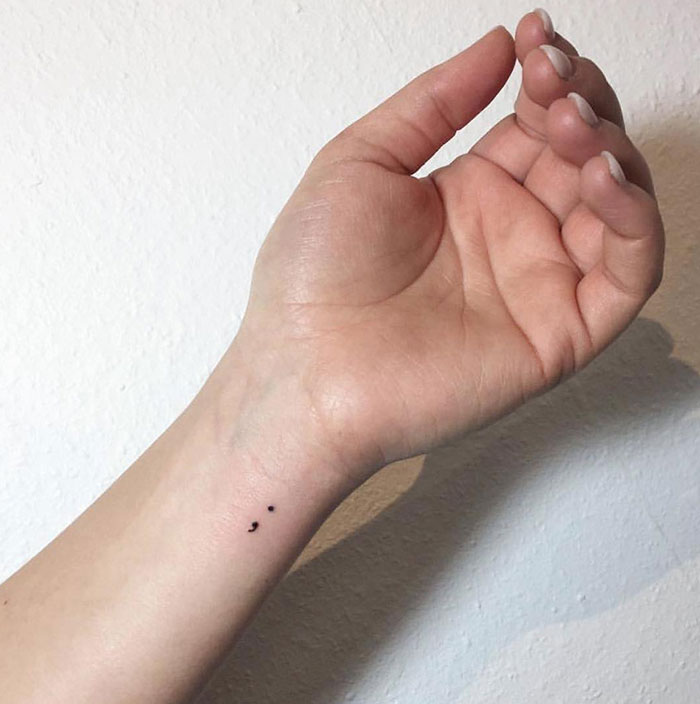 Minimalist semicolon tattoo on inner wrist symbolizing strength and resilience, against a light background.