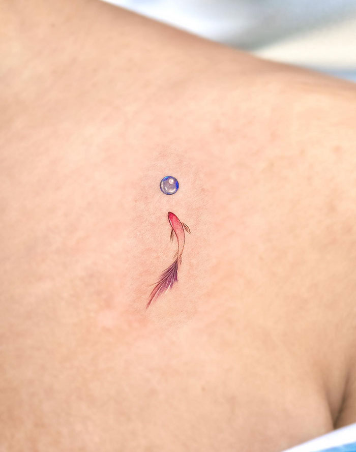 Semicolon tattoo with colorful fish and blue bubble, symbolizing hope and new beginnings on minimalist background.