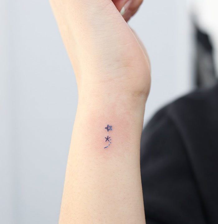 Semicolon tattoo on wrist with blue stars and dots, symbolizing hope and guidance in a celestial design.