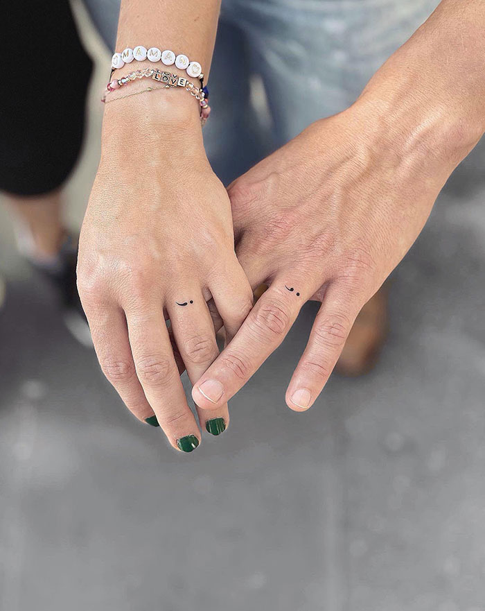 Matching semicolon tattoos on fingers, symbolizing unity and resilience, with bracelets and green nail polish visible.